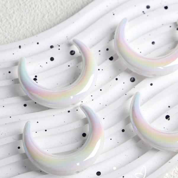 White crescent moon acrylic beads with pastel iridescent reflections on a speckled white tray