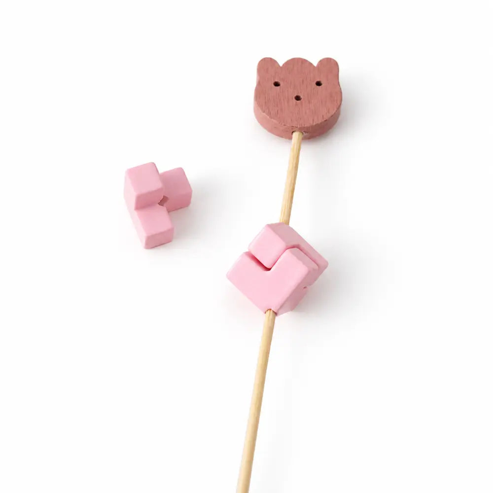 Pink acrylic puzzle bead pieces showing a threading hole and a square assembly on a display rod.