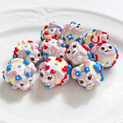 Ten hand-painted acrylic beads with lavender bunny designs, pale yellow bases, red hearts and blue flower details.