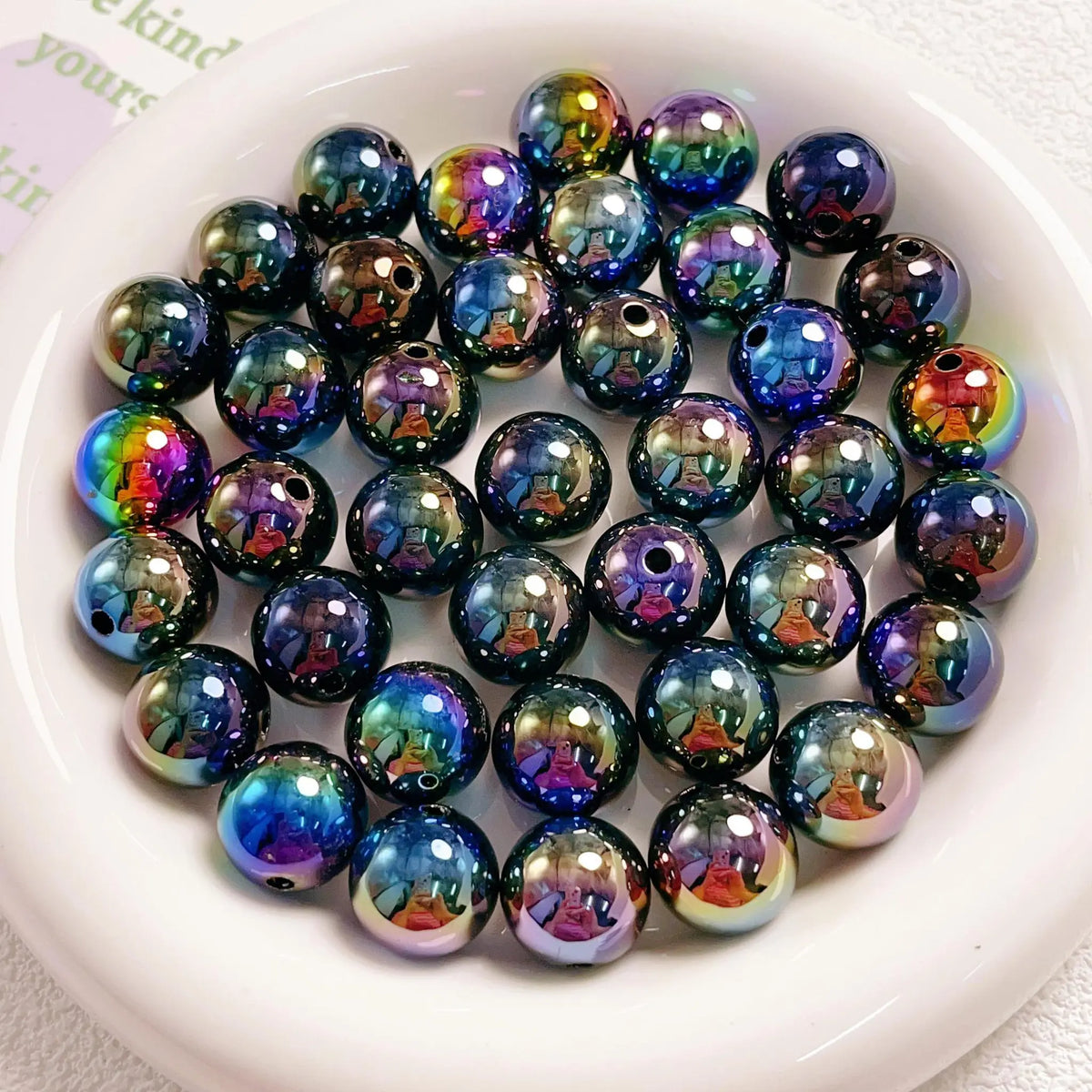 Black acrylic round beads with vivid rainbow reflections and visible stringing holes on a white plate.