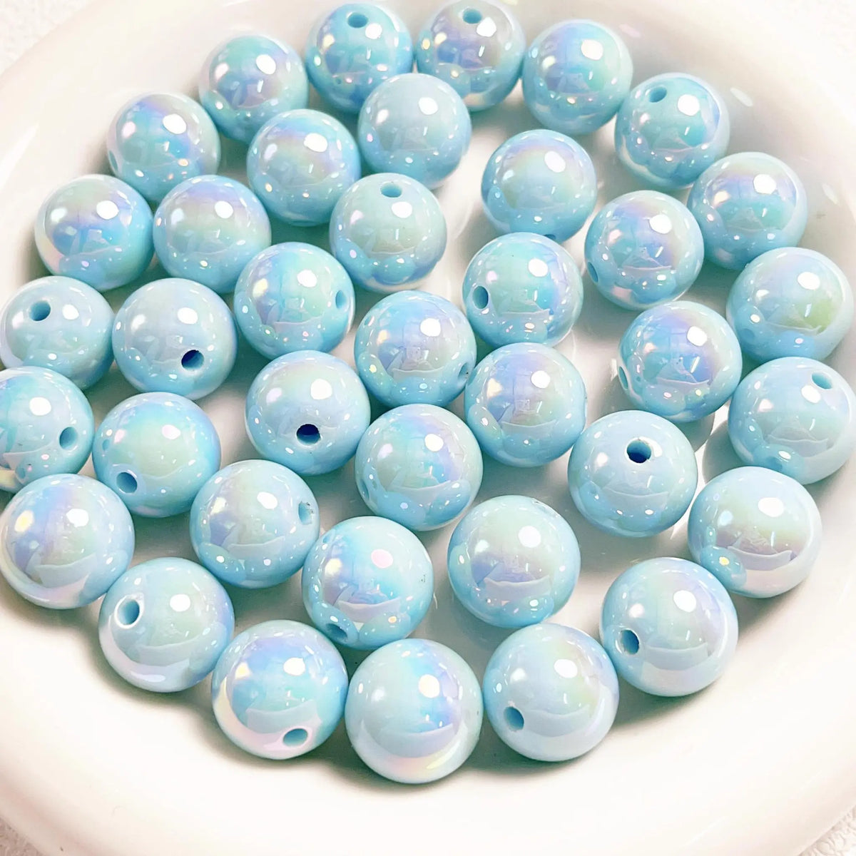 Light blue acrylic round beads with a glossy iridescent finish and visible holes on a white plate.