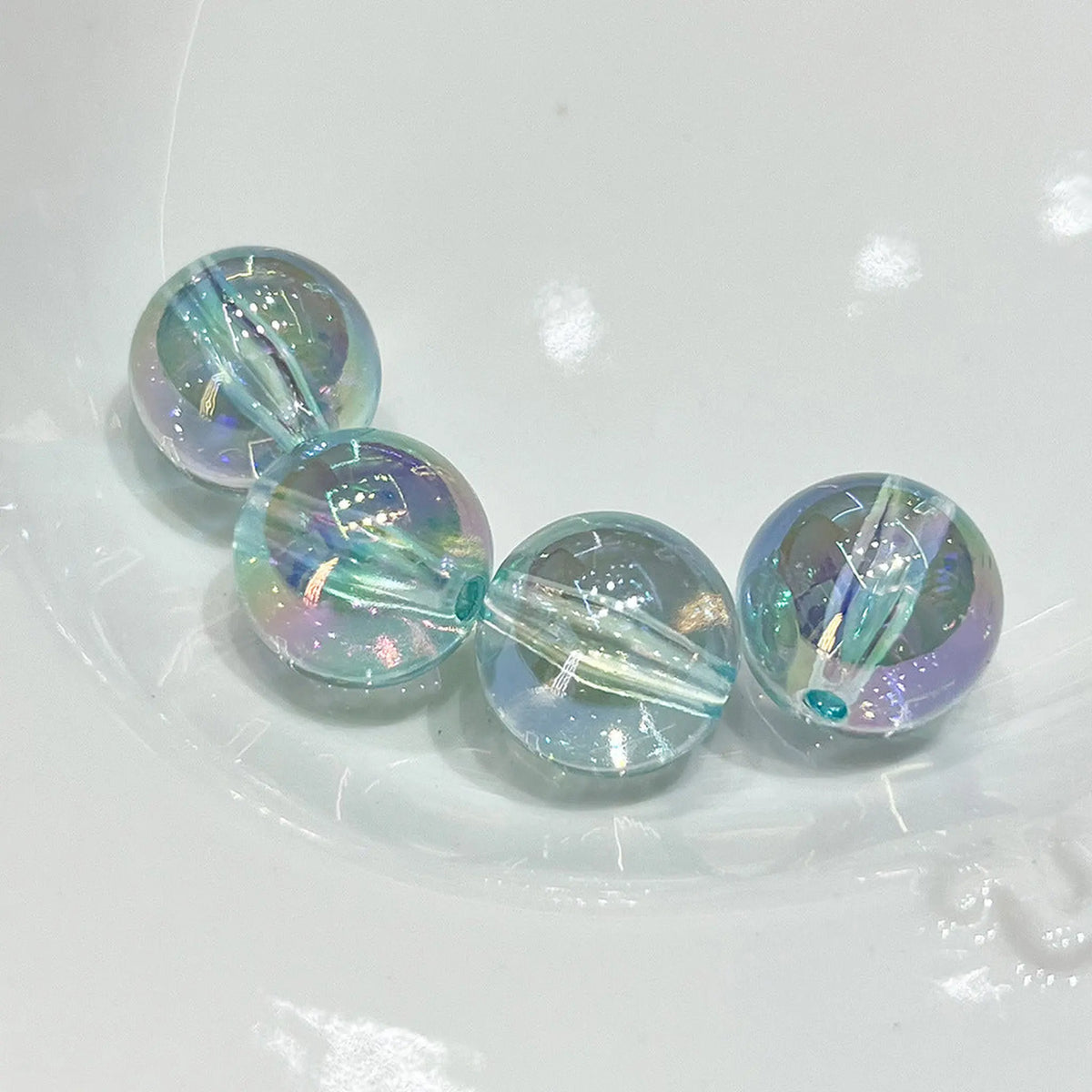 Four transparent blue acrylic round beads with iridescent reflections and visible through-holes.