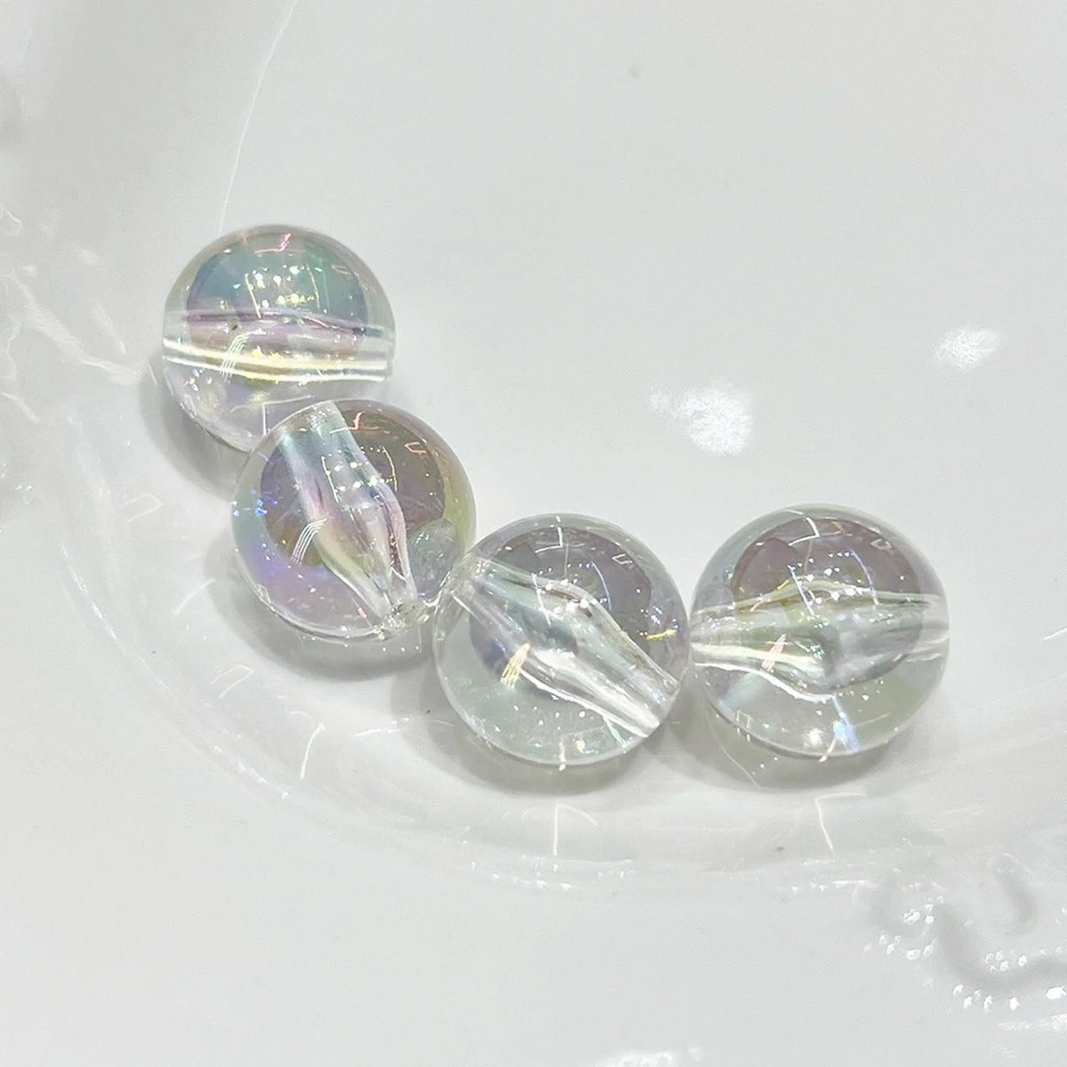 Four clear acrylic round beads with iridescent reflections and visible through-holes on a white plate.