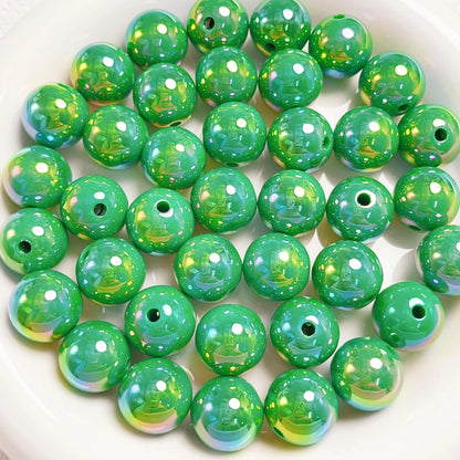 Green acrylic round beads with a glossy iridescent finish and visible stringing holes on a white plate.