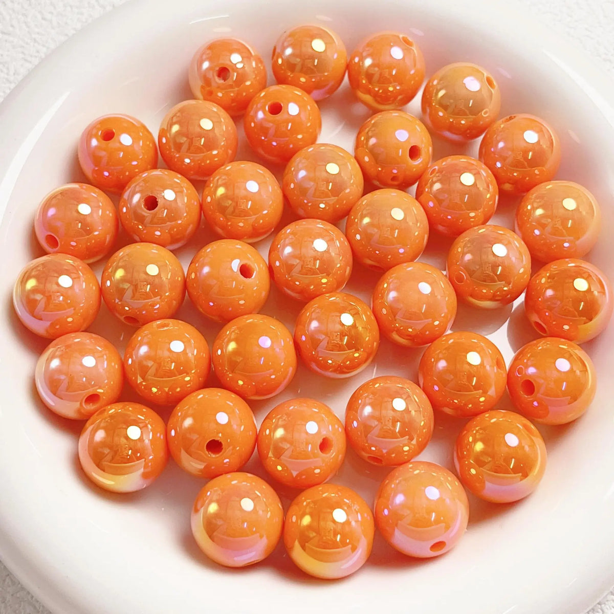 Orange acrylic round beads with a glossy iridescent finish and visible stringing holes on a white plate.