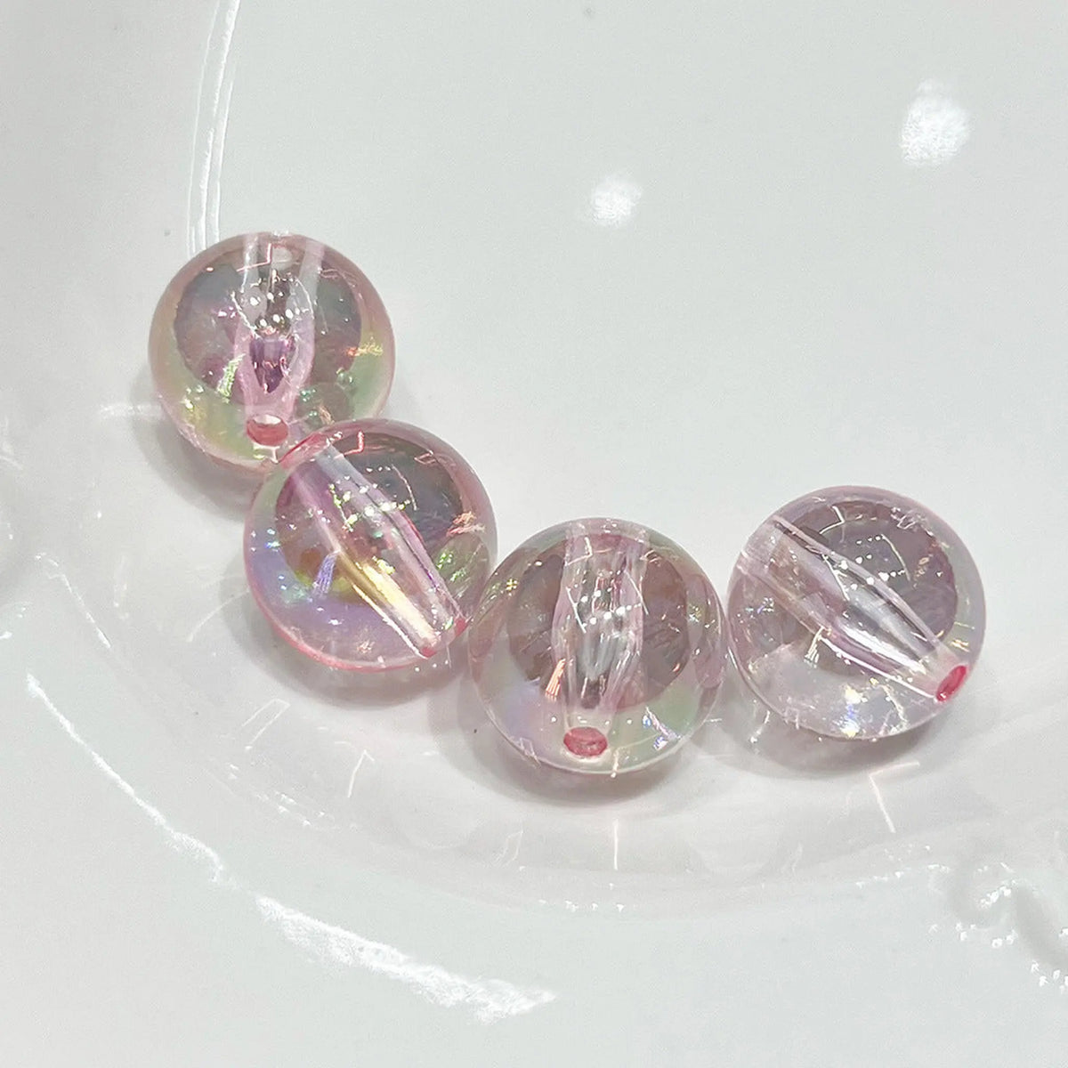 Four transparent pink acrylic round beads with iridescent reflections and visible through-holes.