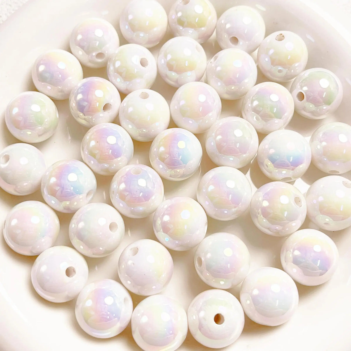 White acrylic round beads with a glossy iridescent finish and visible stringing holes on a white plate.