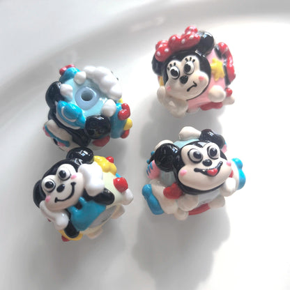 Four hand-painted acrylic beads showing black and white faces, pink and blue decorations and a threading hole.