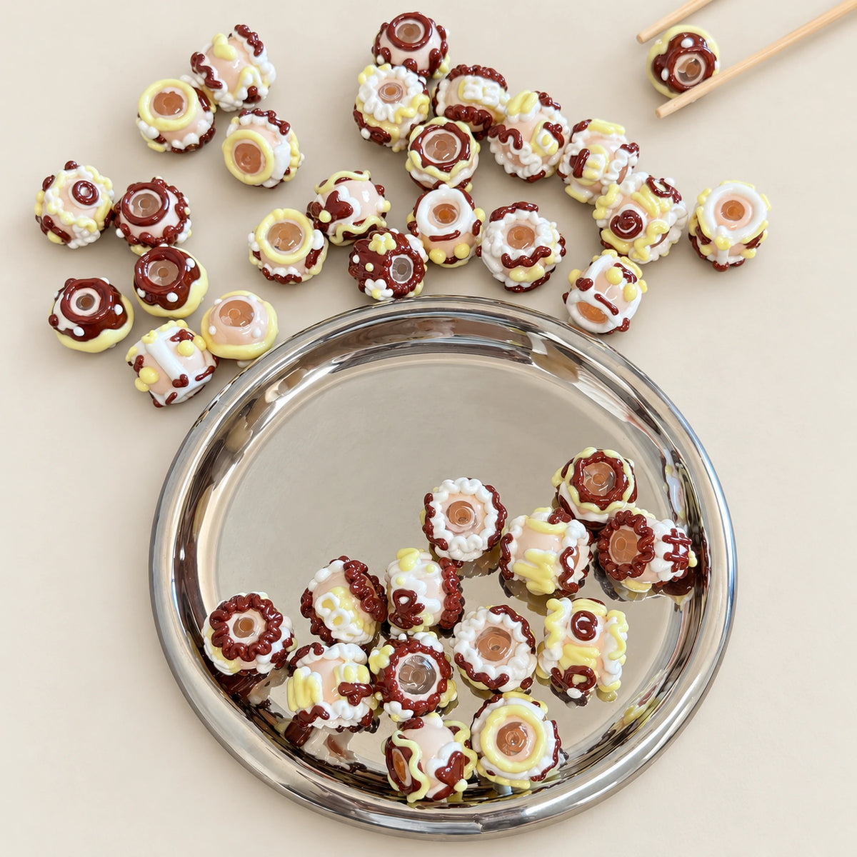 Assorted cocoa brown and white hand painted 3D beads displayed in a silver dish