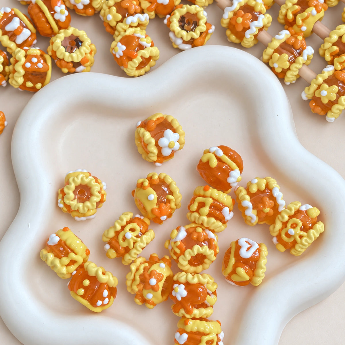 Jelly orange hand-painted 3D beads with yellow raised decorations and white flower motifs displayed in a white tray