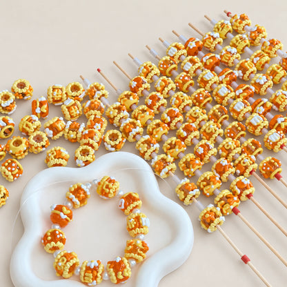 Orange jelly and yellow hand-painted decorative craft beads in tray with threaded display rods and an example bracelet